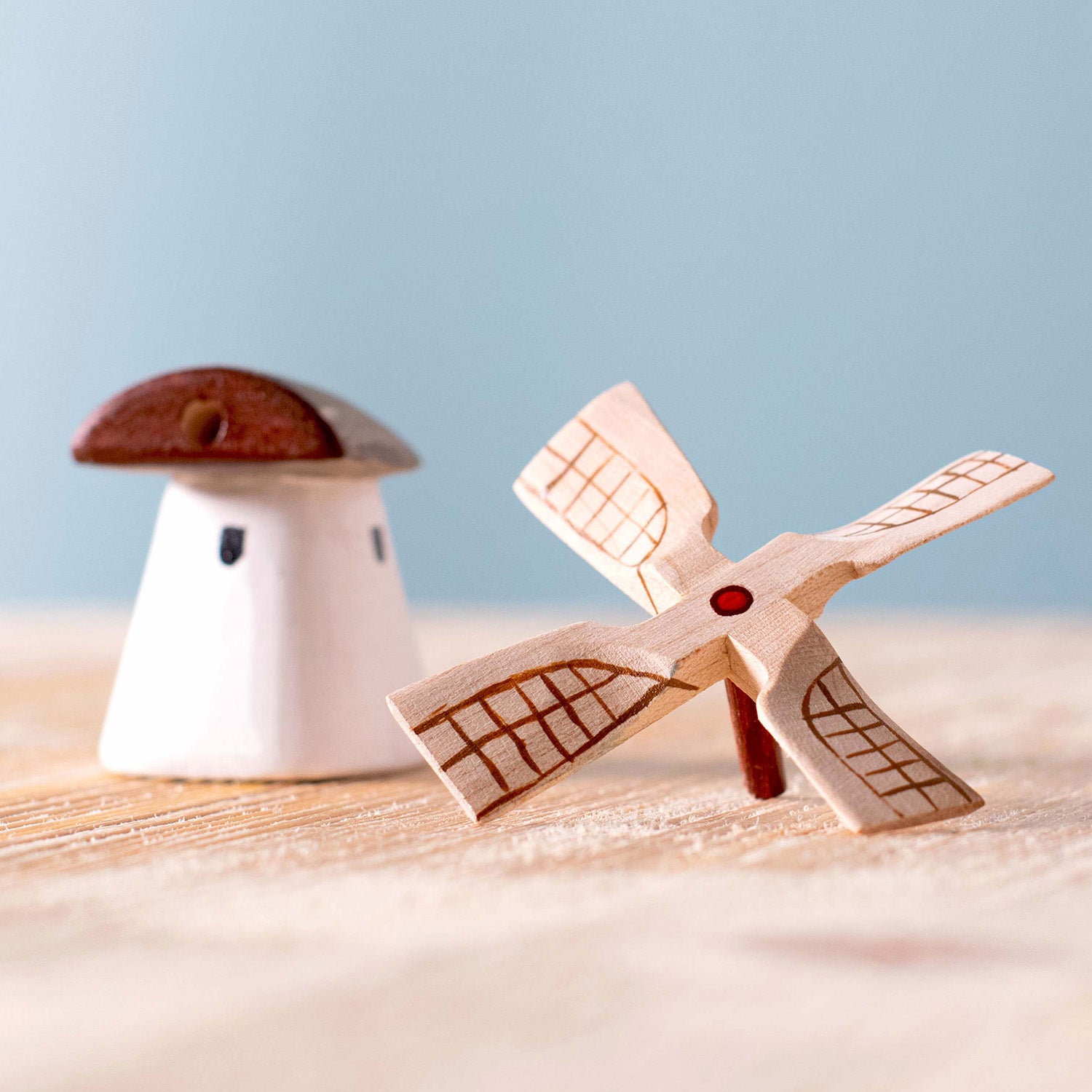 Bumbu Miniature Wooden Moldova Windmill. The toy sits on a wooden surface against a blue background. An adult hand is in view to show scale.