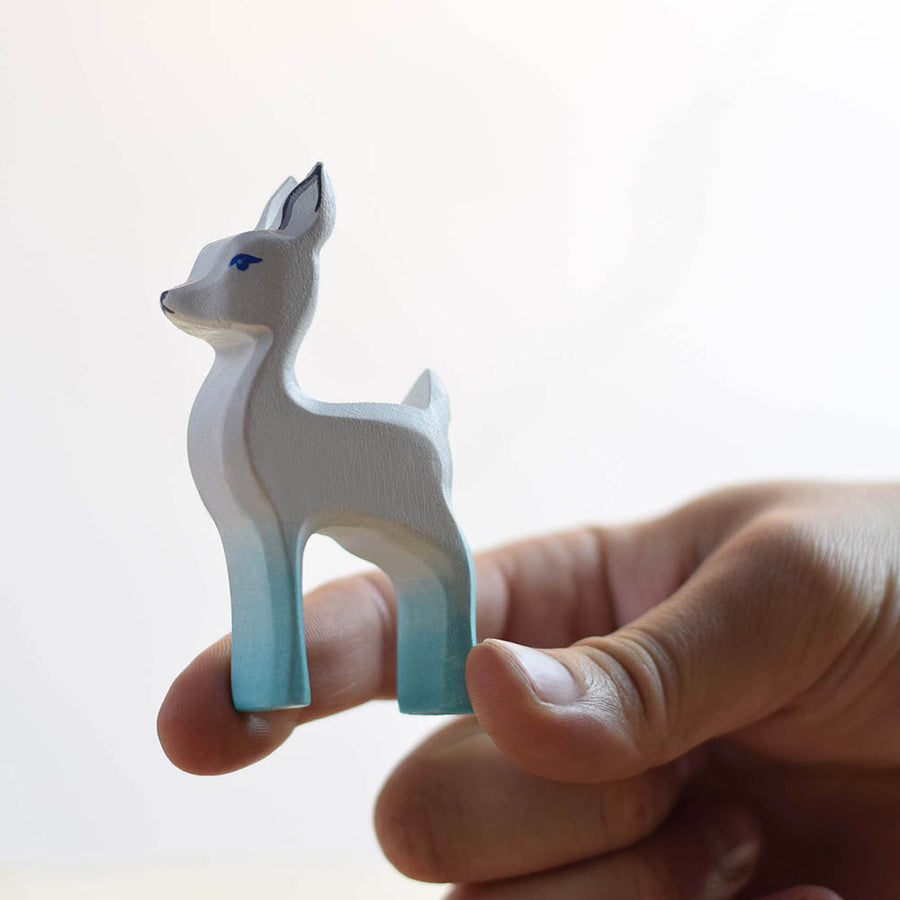 Close up of a hand holding the Bumbu plastic-free white fawn toy figure on a white background