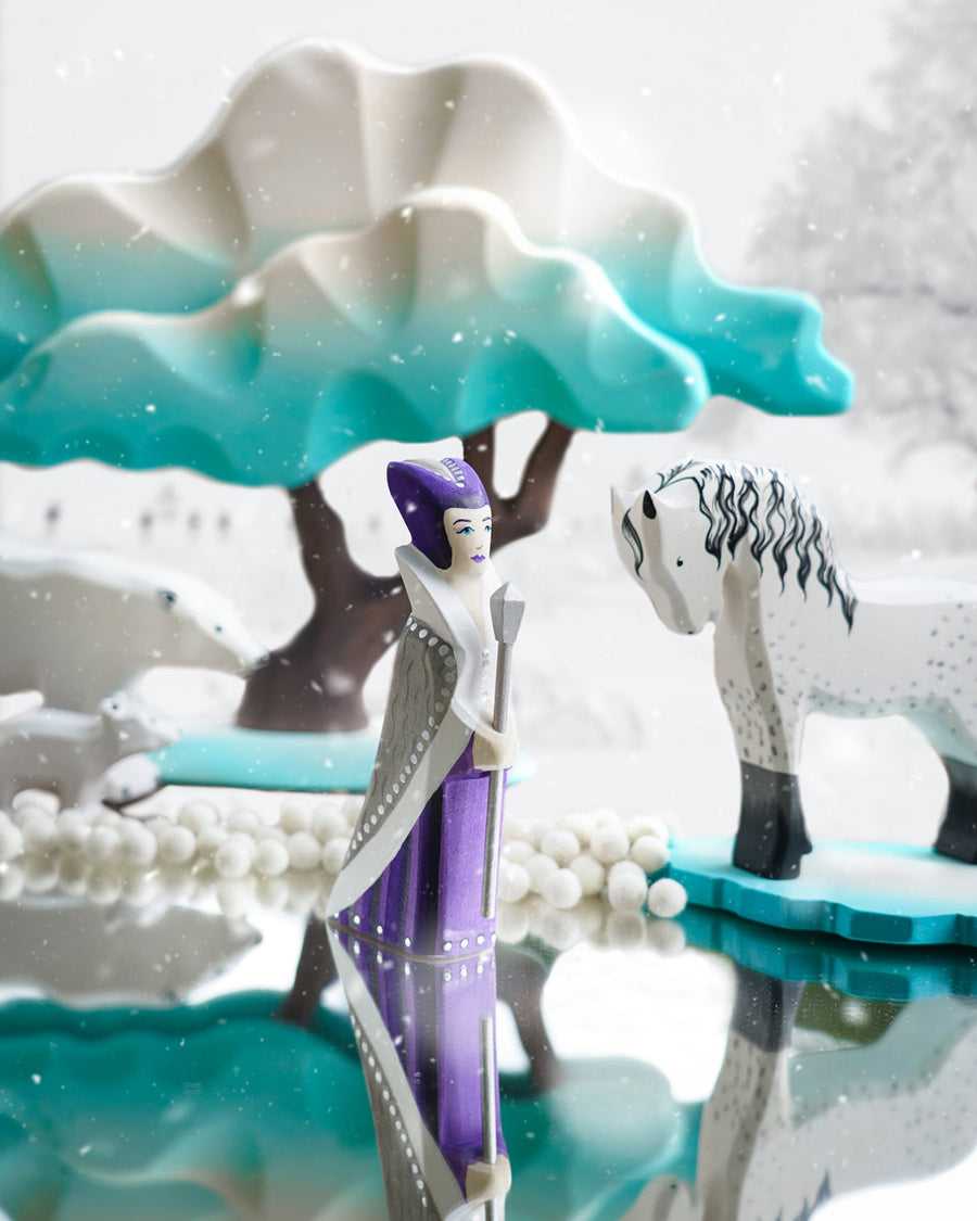 Bumbu wooden snow queen toy figure stood on a mirror next to a white horse figure and a Bumbu winter maple tree