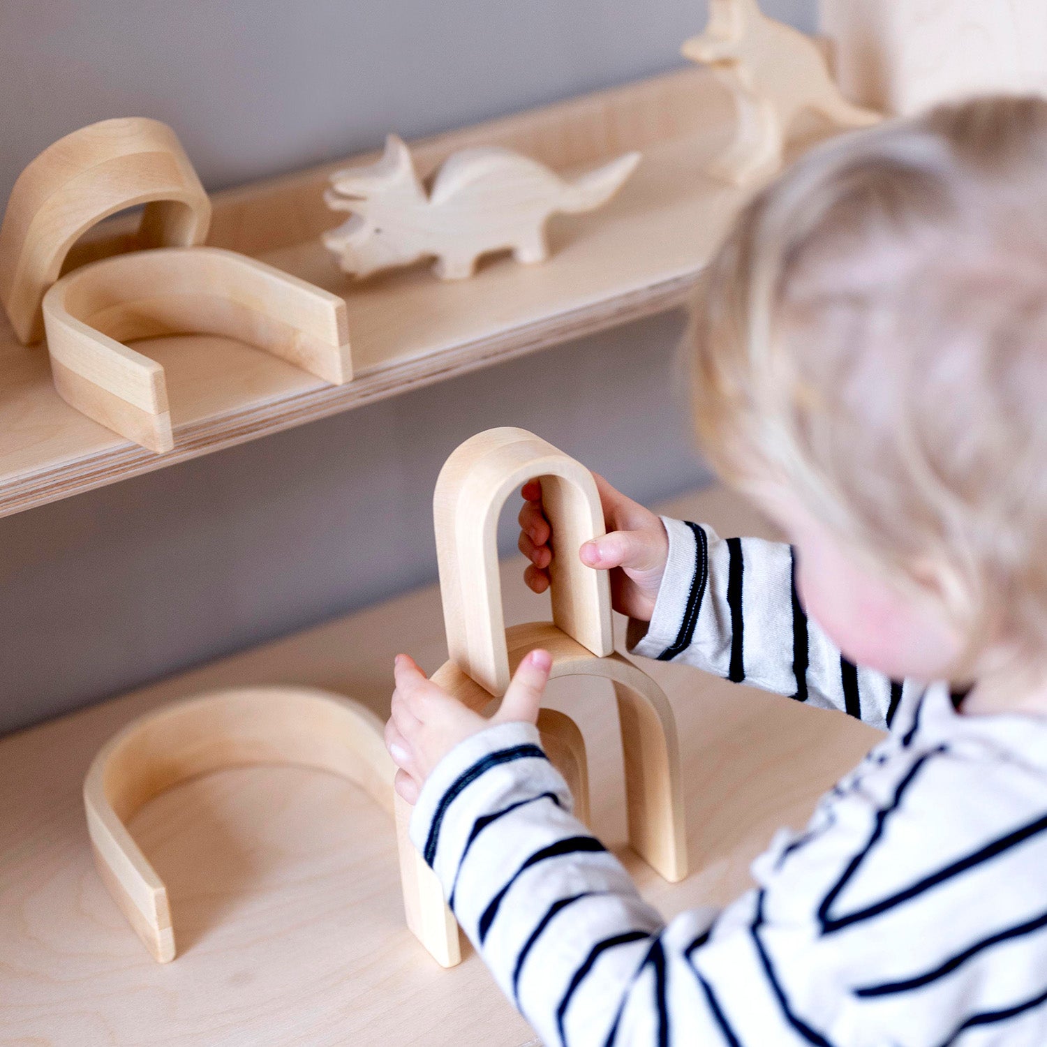 Bumbu Natural Wooden Stacking Arches. The toy sits on a wooden surface against a blue background.