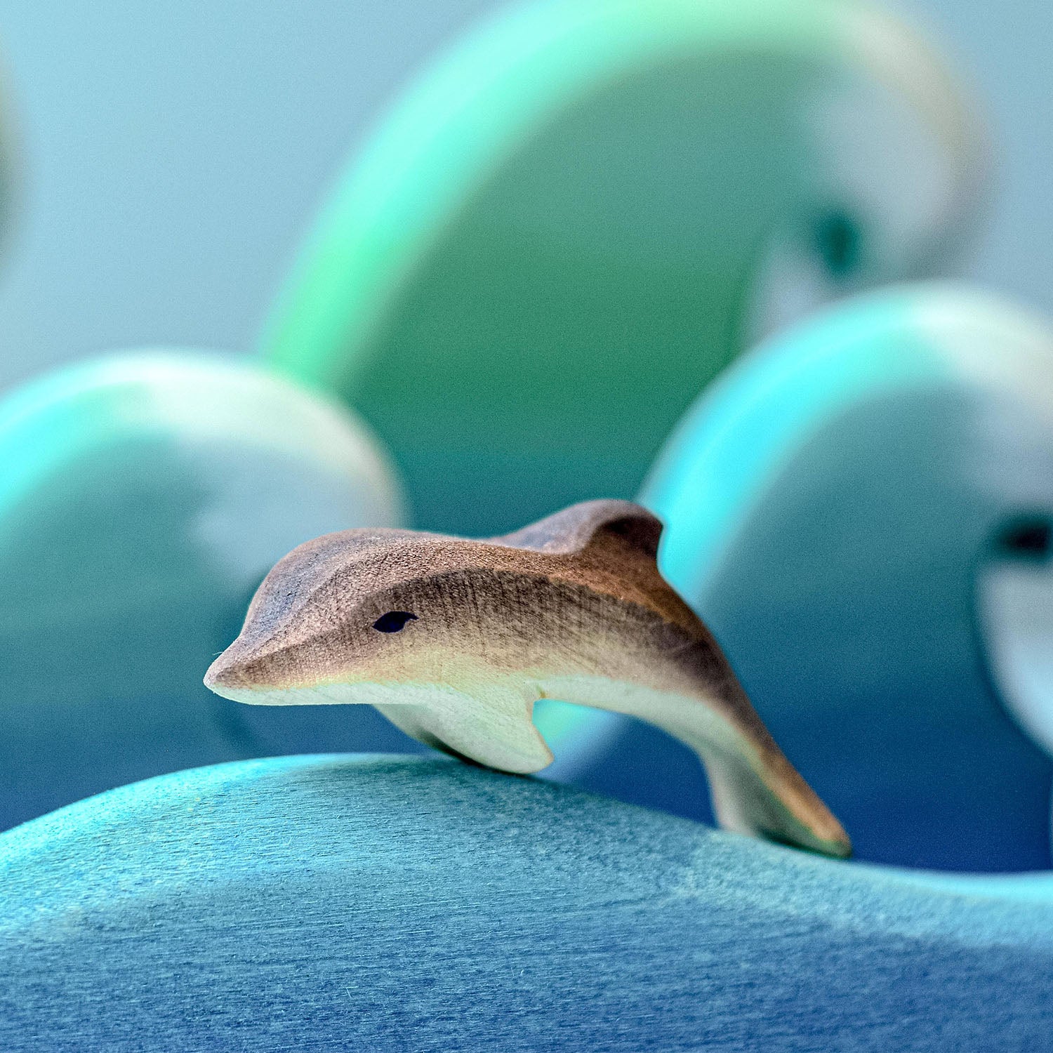 Bumbu Wooden Baby Dolphin. The toy is paired with a set of waves and several adult dolphins.