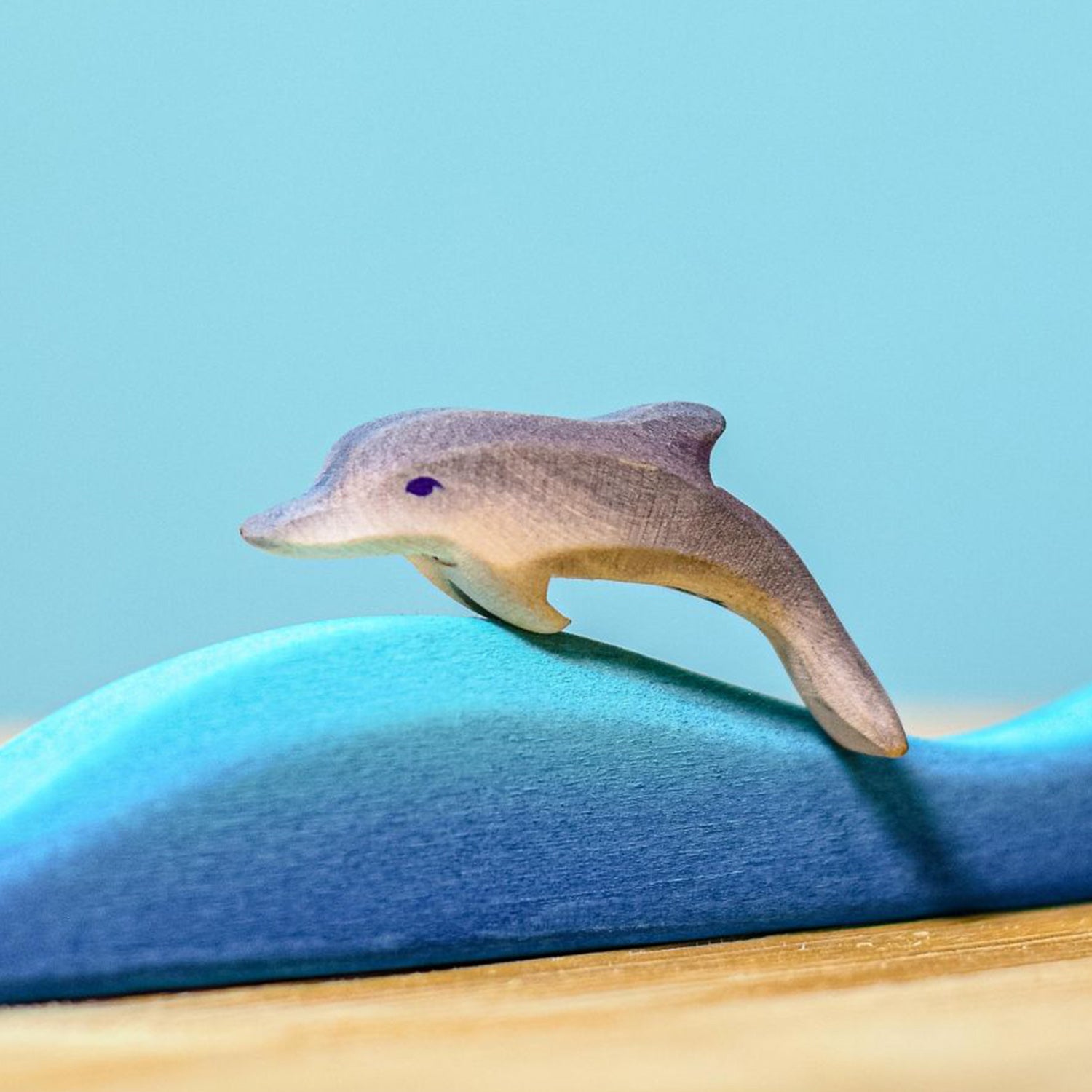 Bumbu Wooden Baby Dolphin. The toy is paired with a wave and sits on a wooden surface against a blue background.