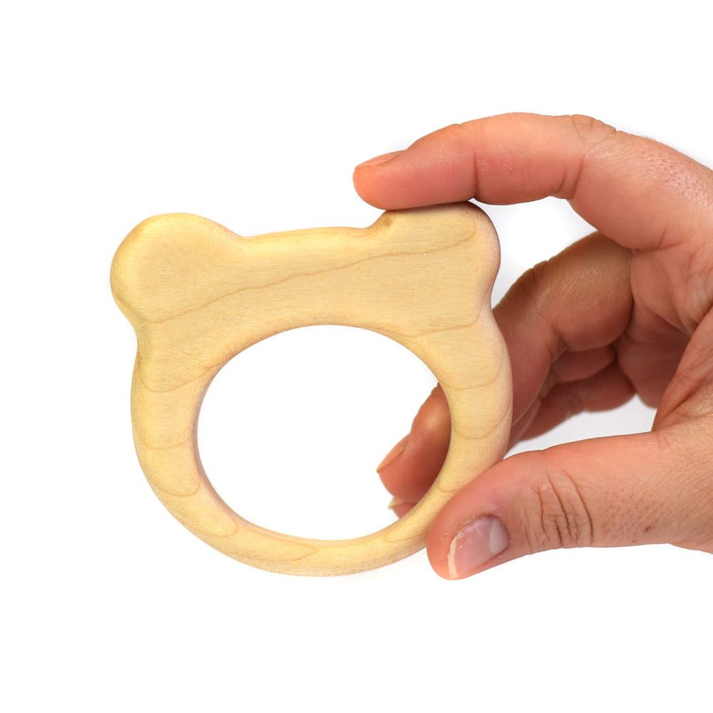 Close up of a hand holding the Bumbu plastic-free wooden bear baby teether on a white background