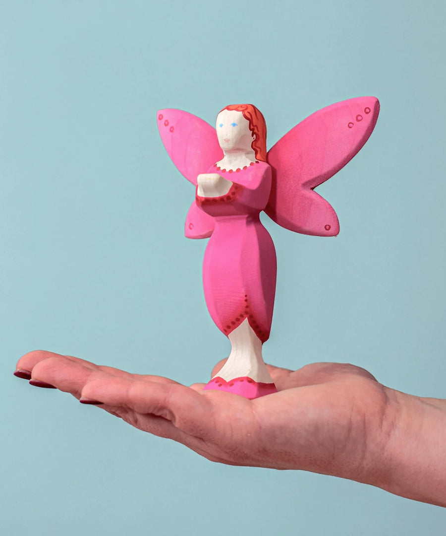 An adult balancing a Bumbu Wooden Blossom Fairy on their hand against a blue background.