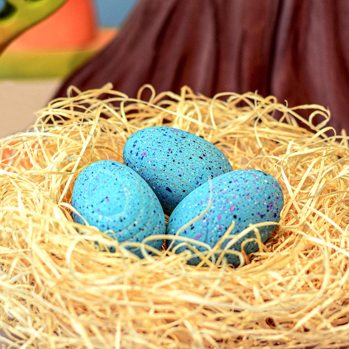 Three Wooden Bumbu Brontosaurus nestled in the palm of a persons hand on a blue background. The eggs show the natural wood grain and smooth finish of the eggs