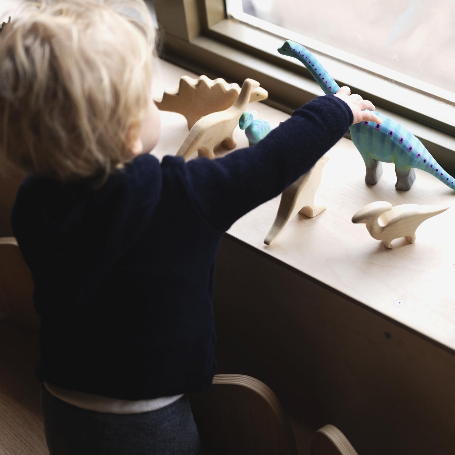 A child playing with the Bumbu Brontosaurus toys on a window sill