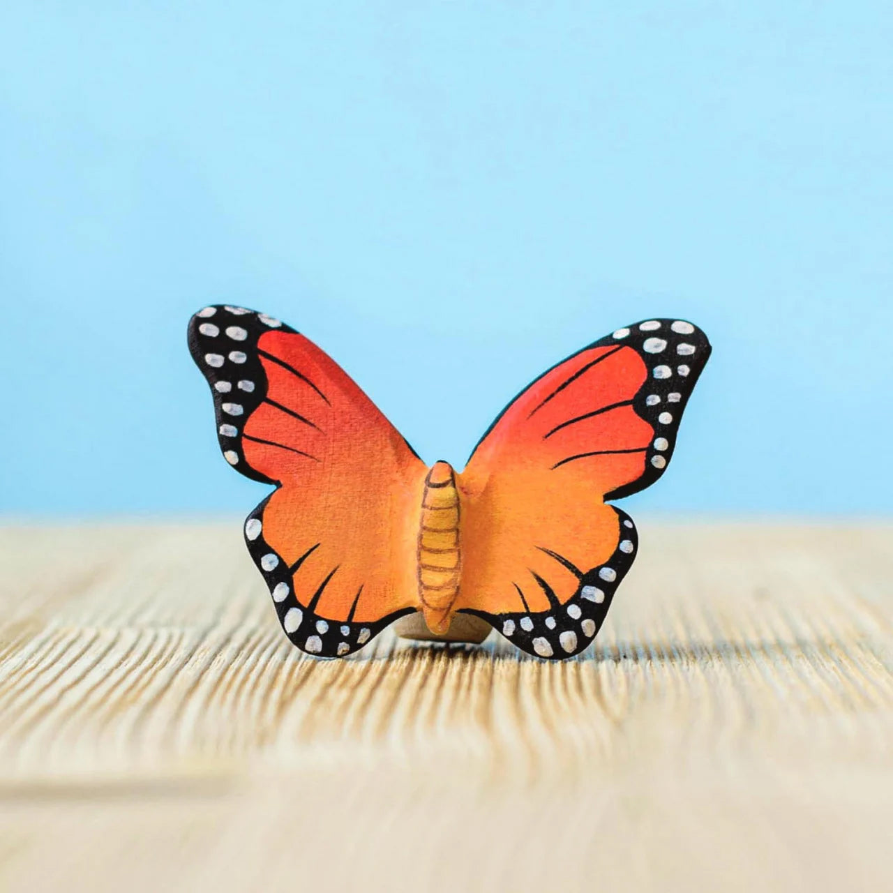 Bumbu Wooden Butterfly Figure pictured on a wooden surface with a blue background 