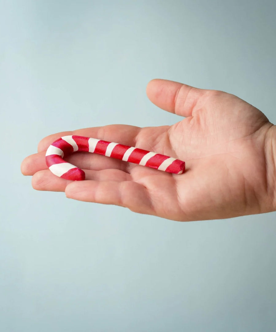 A hand holding the red and white wooden Bumbu candy cane