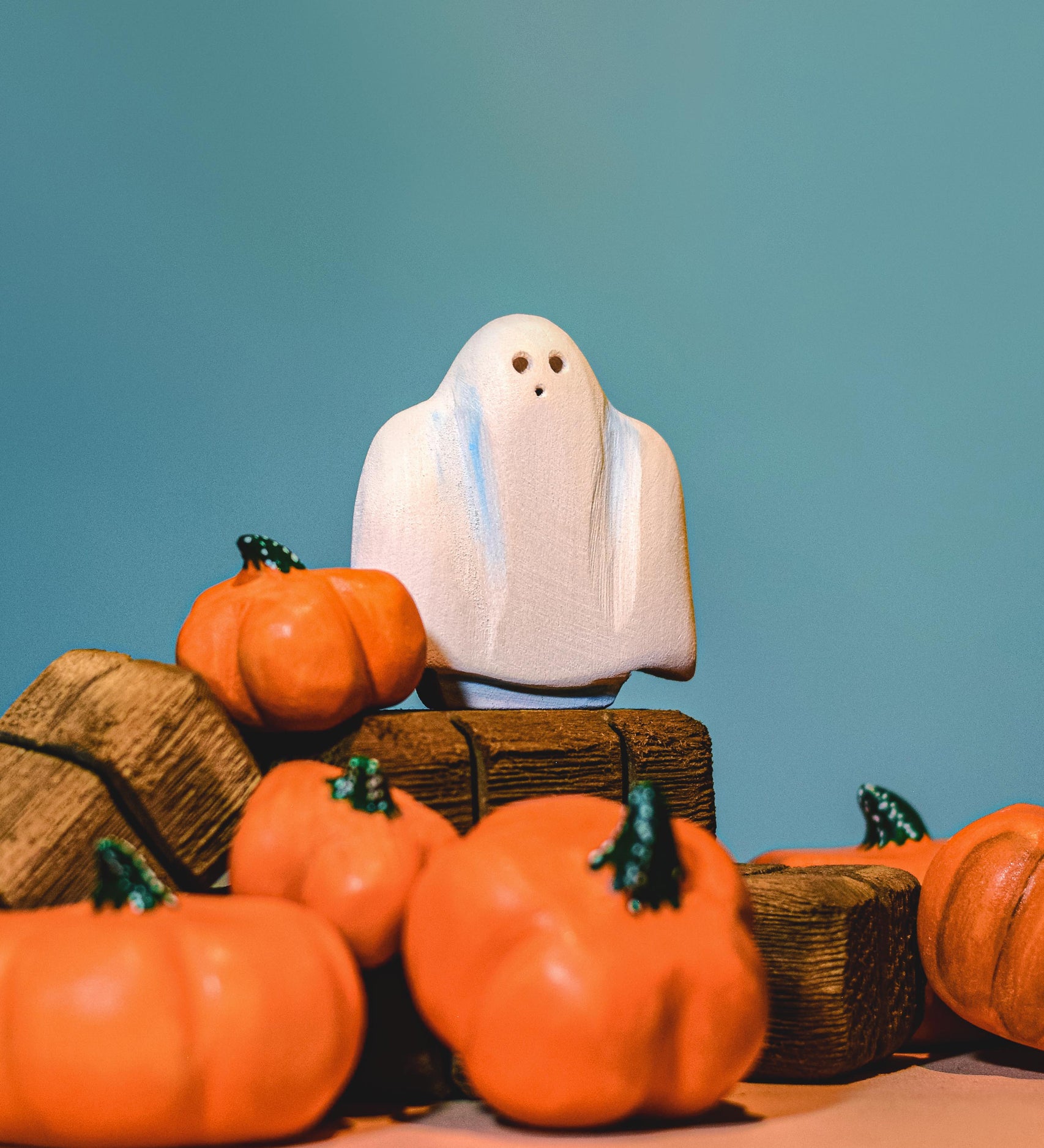 A wooden Bumbu ghost figure placed on wooden hay bales surrounded by wooden pumpkin figures.