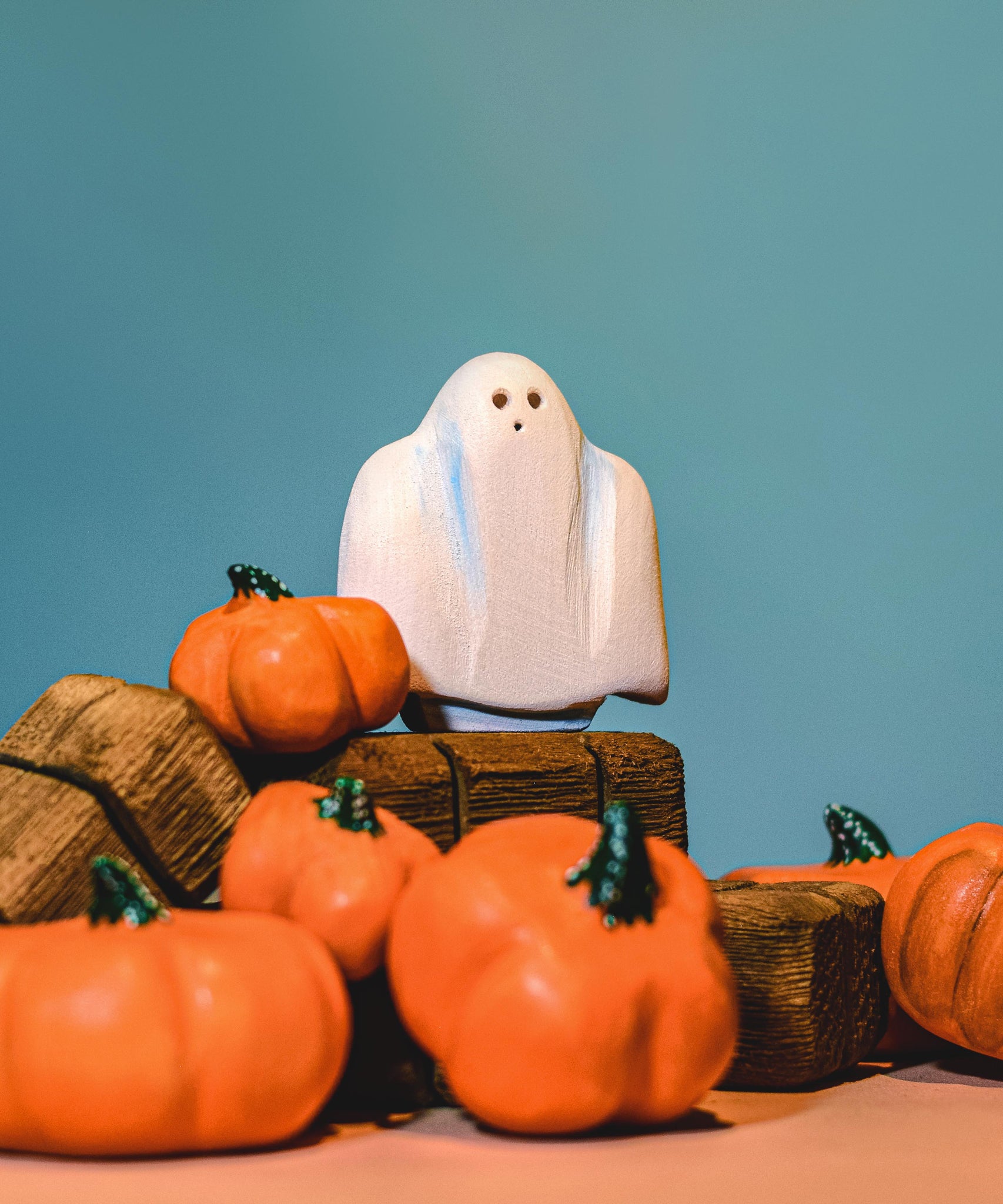 A wooden Bumbu ghost figure placed on wooden hay bales surrounded by wooden pumpkin figures.