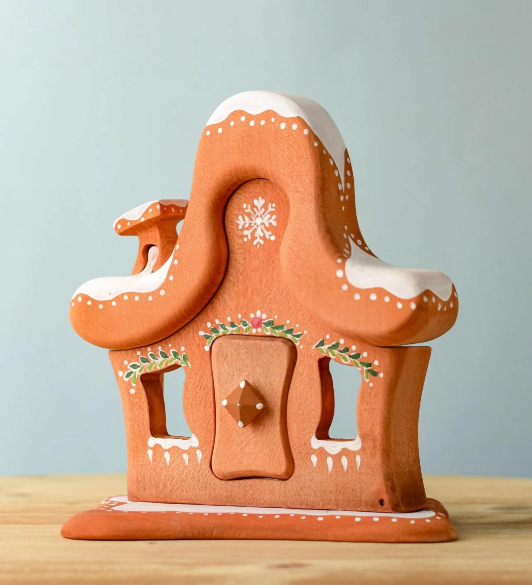 A wooden Bumbu gingerbread house with white hand painted snow and holy above the door and windows