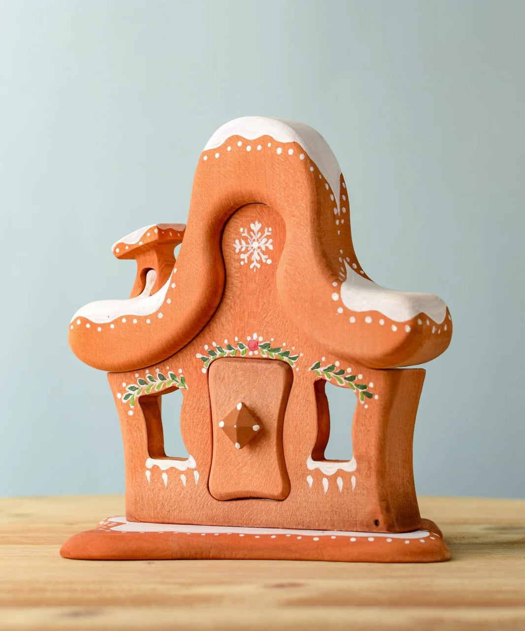 A wooden Bumbu gingerbread house with white hand painted snow and holy above the door and windows