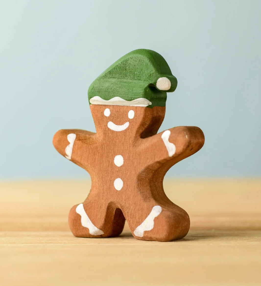 A wooden Bumbu gingerbread cookie boy with hand painted white detailing and wearing a green hat