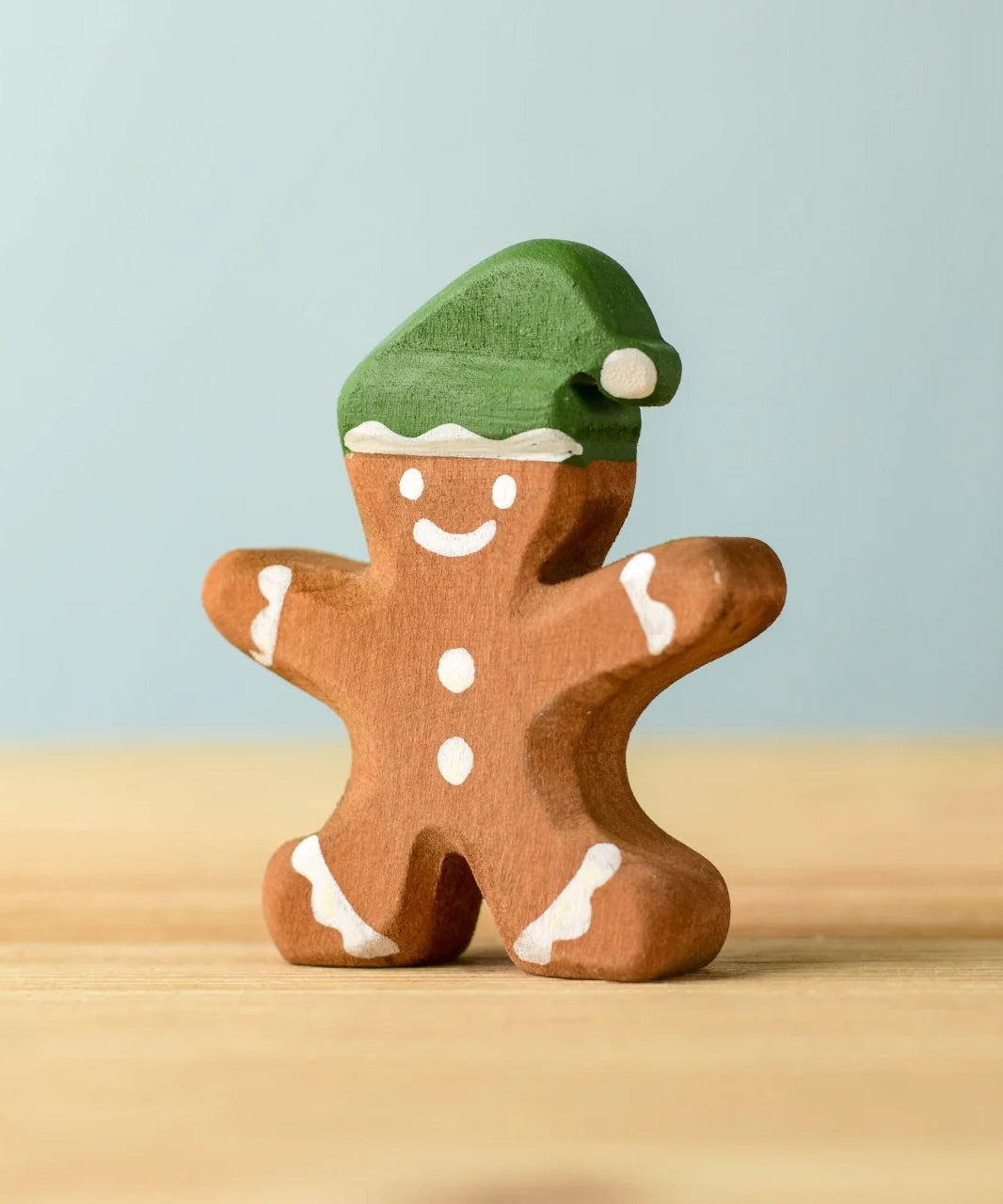 A wooden Bumbu gingerbread cookie boy with hand painted white detailing and wearing a green hat