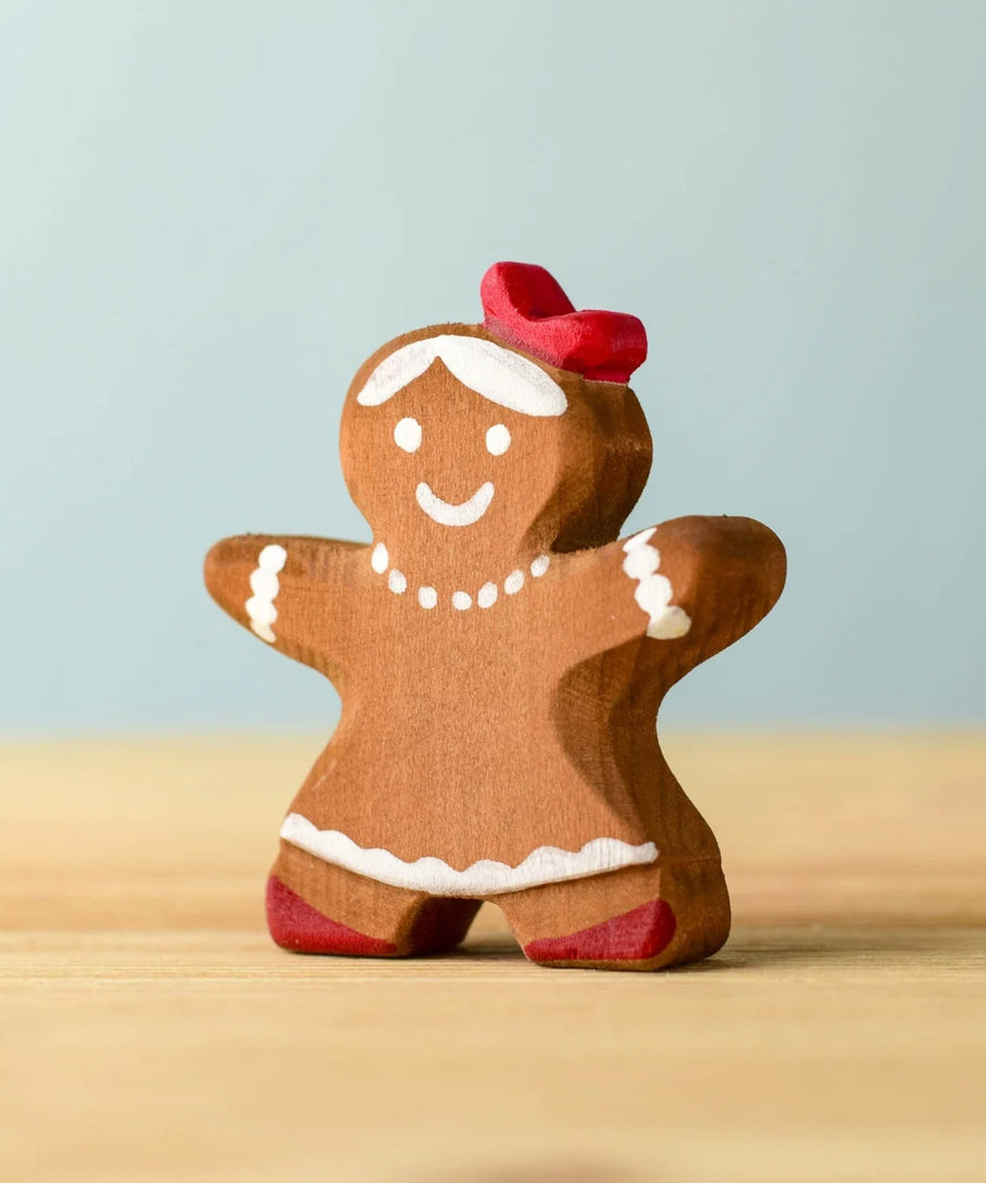 A wooden Bumbu gingerbread cookie girl with hand painted white detailing wearing a red bow on her head 