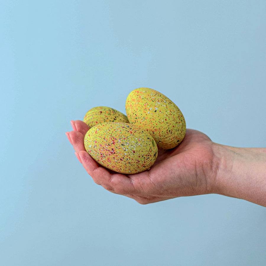 A speckled Yellow Wooden Bumbu Stegosaurus Egg being held in a persons hand