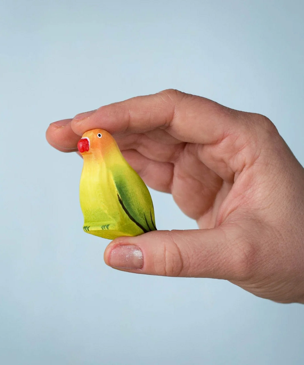 Bumbu wooden blue lovebird figure held by an adult hand