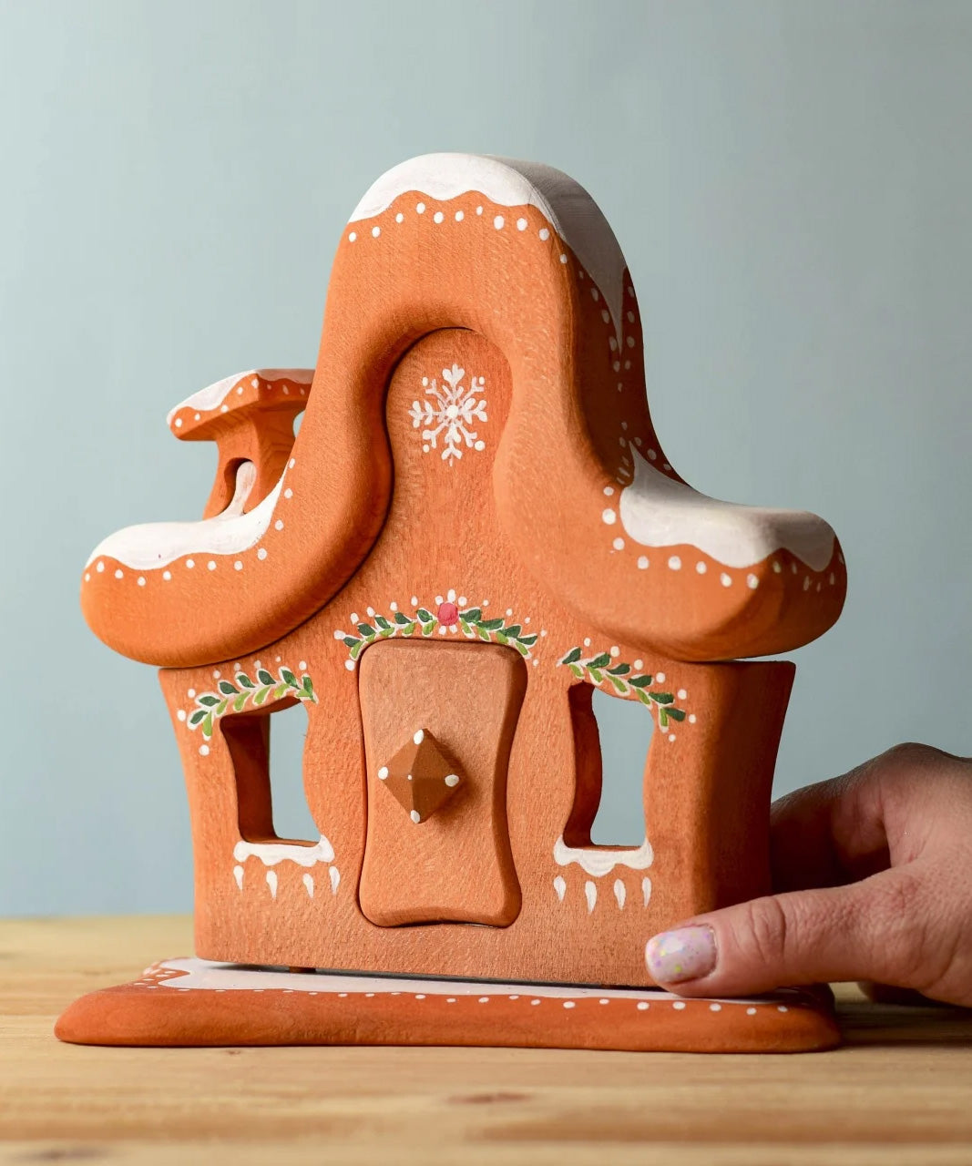 A hand next to the Bumbu wooden gingerbread house for size .