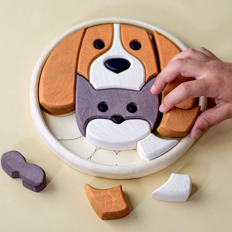 Wooden circular block puzzle with colourful pieces in various shapes forming an image of a cat and dog. Most of the puzzle is complete with three sections remaining to fill. There is an adult hand in the photo to show the scale of the puzzle.