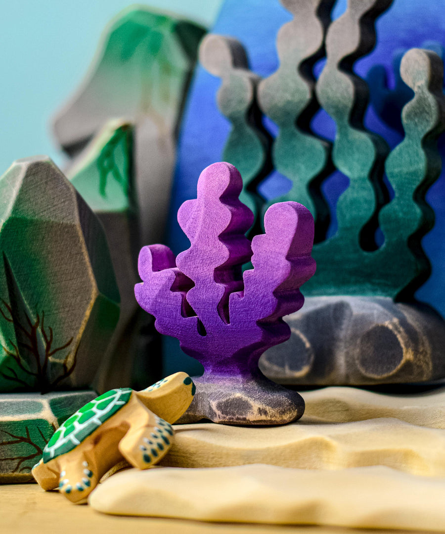 A purple Bumbu seaweed figure placed in a samll world play set up surrounded by other varieties of seaweed and rocks