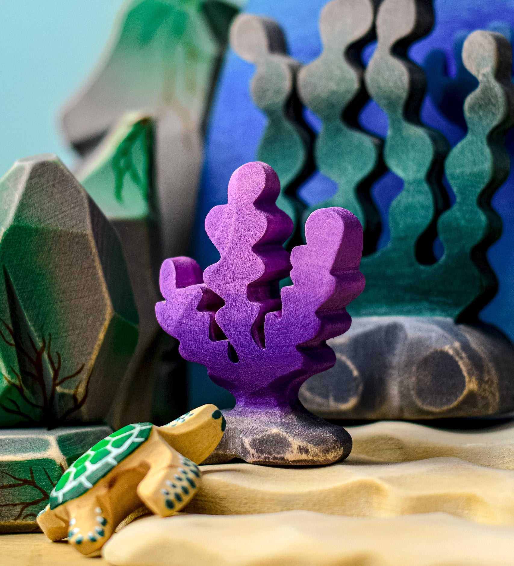 A purple Bumbu seaweed figure placed in a samll world play set up surrounded by other varieties of seaweed and rocks