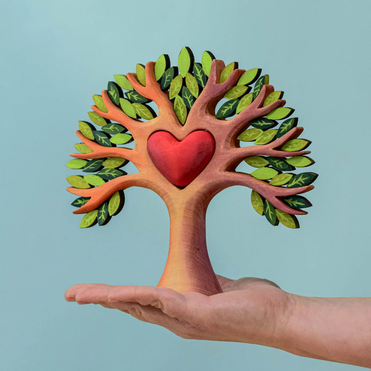 with a removable wooden red heart next to the tree. The tree is displayed on a wooden table with a blue backg