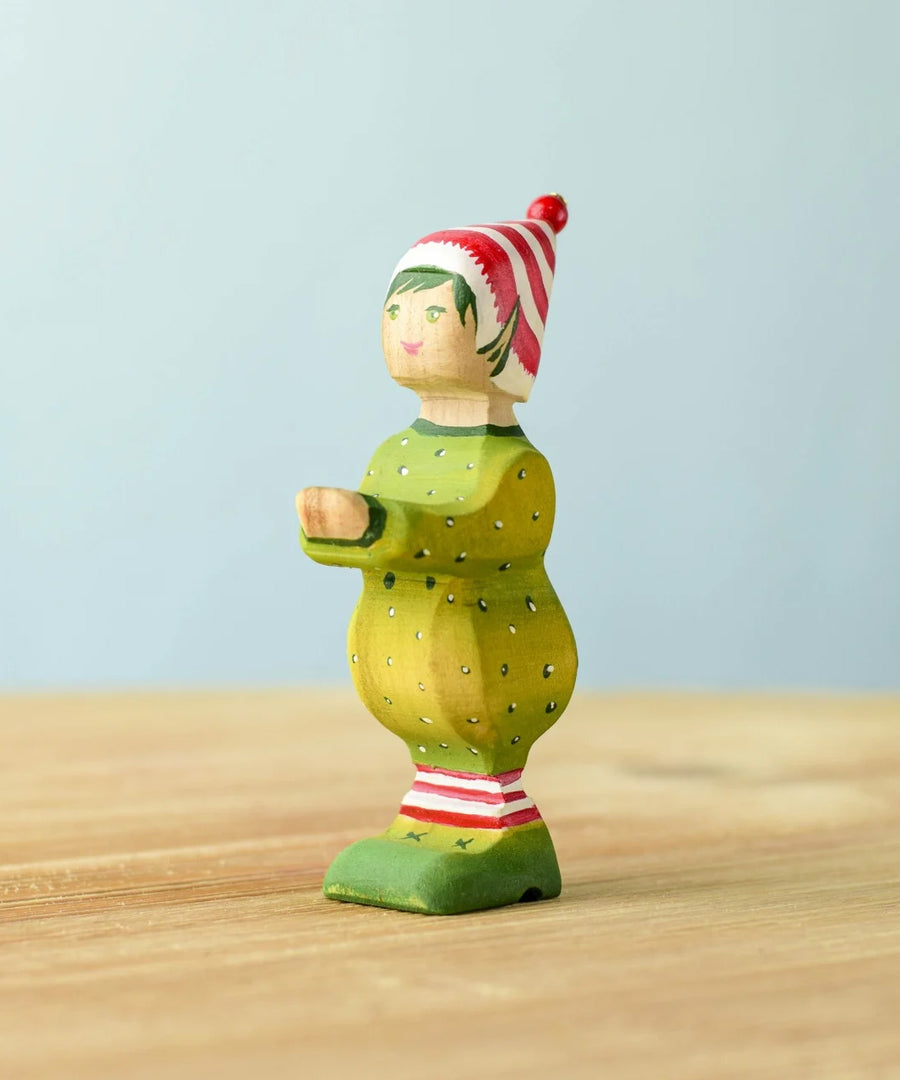 A wooden Bumbu Santas elf wearing a red and white striped hat and a green outfit with its hands holding out to carry presents.