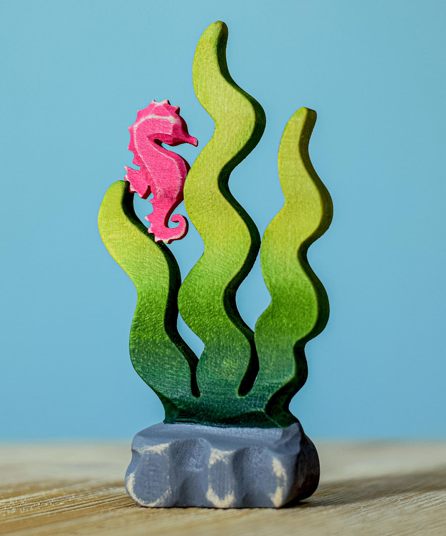 A bumbu wooden seahorse figure perched on green Bumbu sugar kelp seaweed