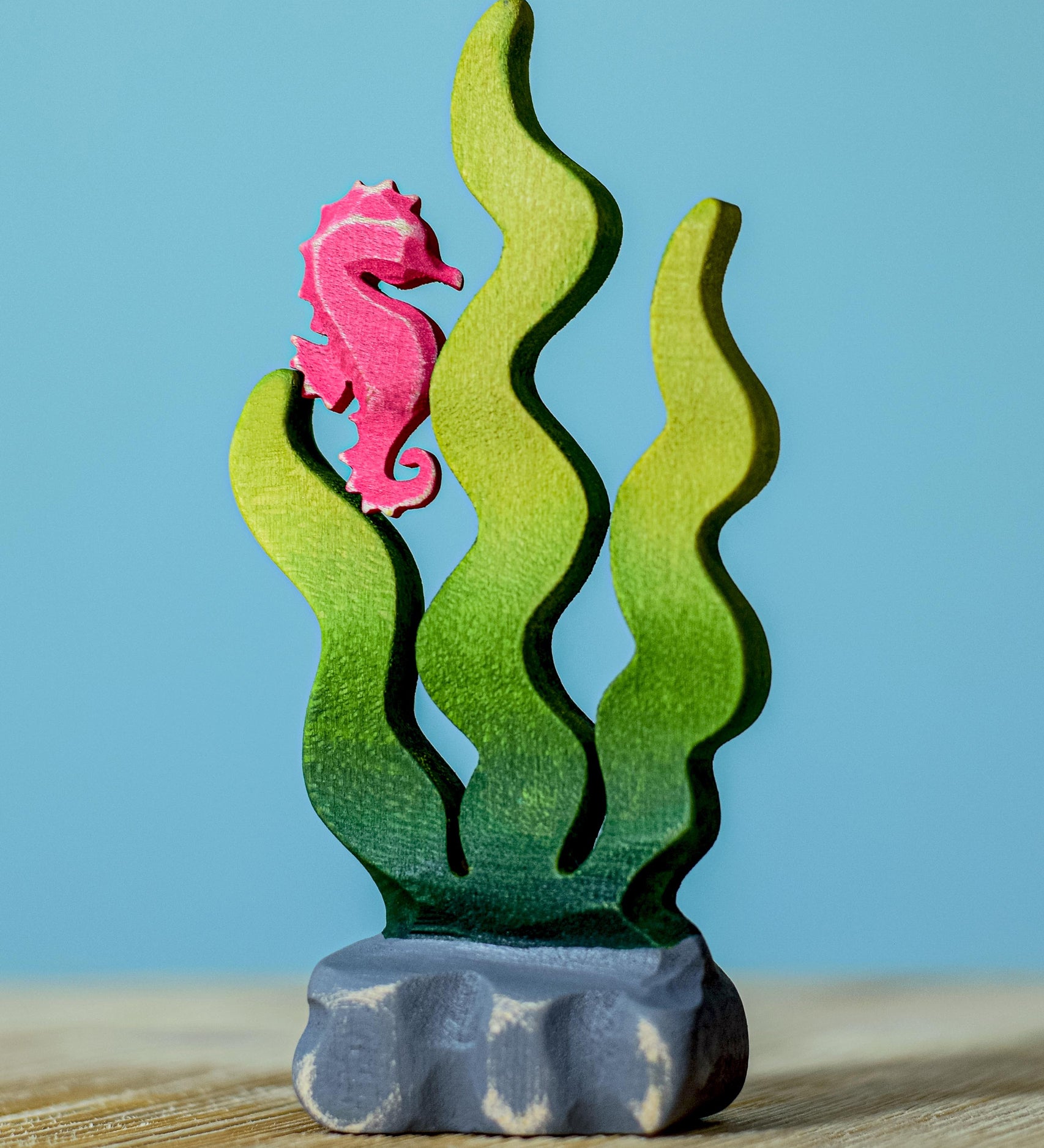 A bumbu wooden seahorse figure perched on green Bumbu sugar kelp seaweed