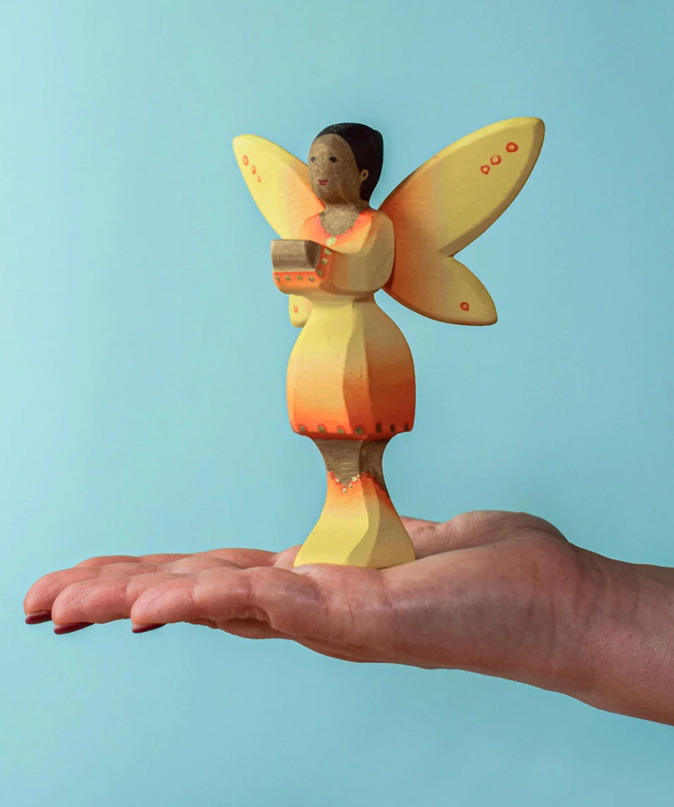 An adult balancing a Bumbu Wooden Sunflower Fairy on their hand against a blue background.