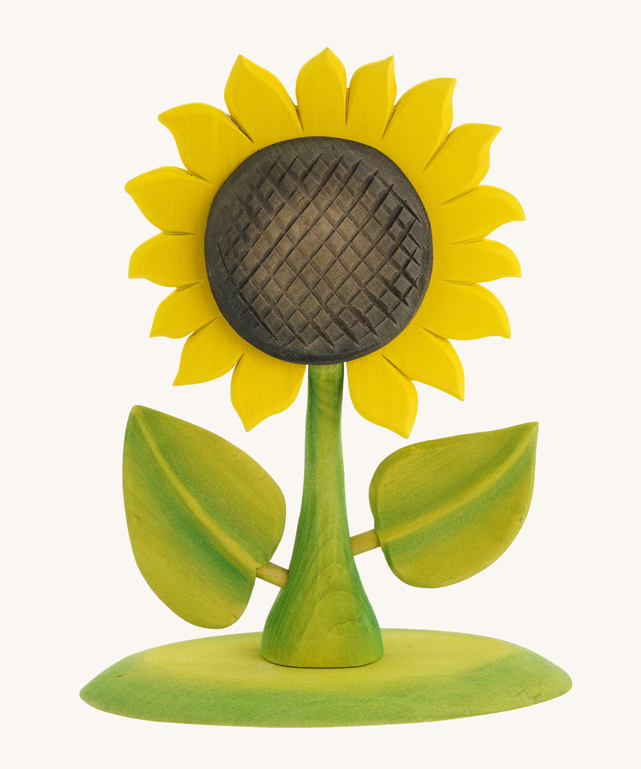 Bumbu Large Wooden Sunflower, Hand Crafted and Hand Painted. A Large yellow Sunflower with green stalk and leaves, on a green wooden base being held in a hand. On a blue background