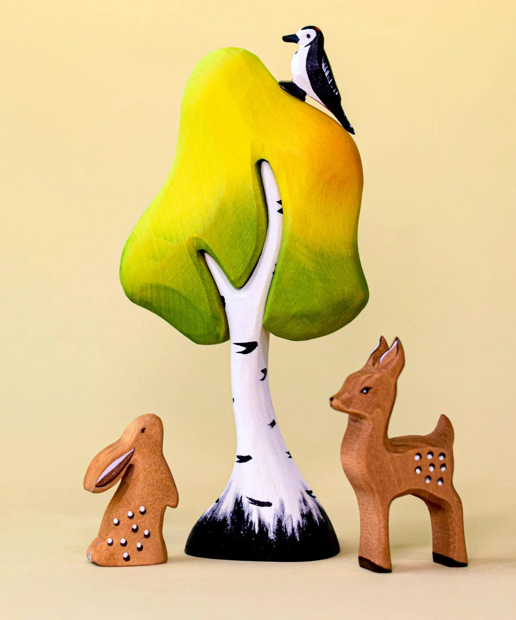 A small wooden Bumbu tree with a rabbit and fawn stood underneath. A wooden woodpecker is perched on top. 