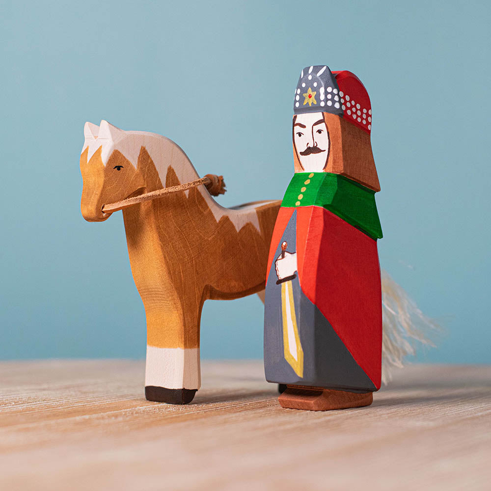 Bumbu Vlad the Dracula impaler toy figure stood on a wooden background next to a brown toy horse