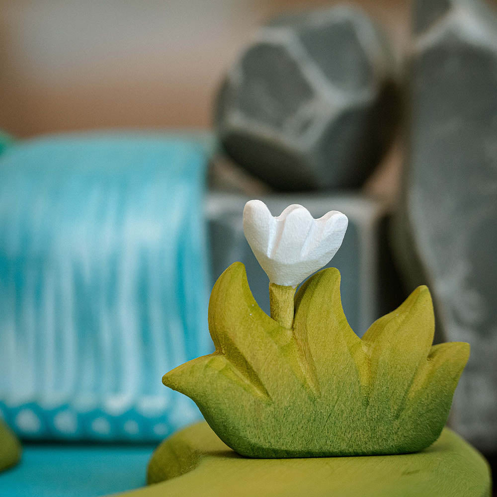 Close up of the Bumbu plastic-free wooden grass toy with white flower on a small world waterfall scene