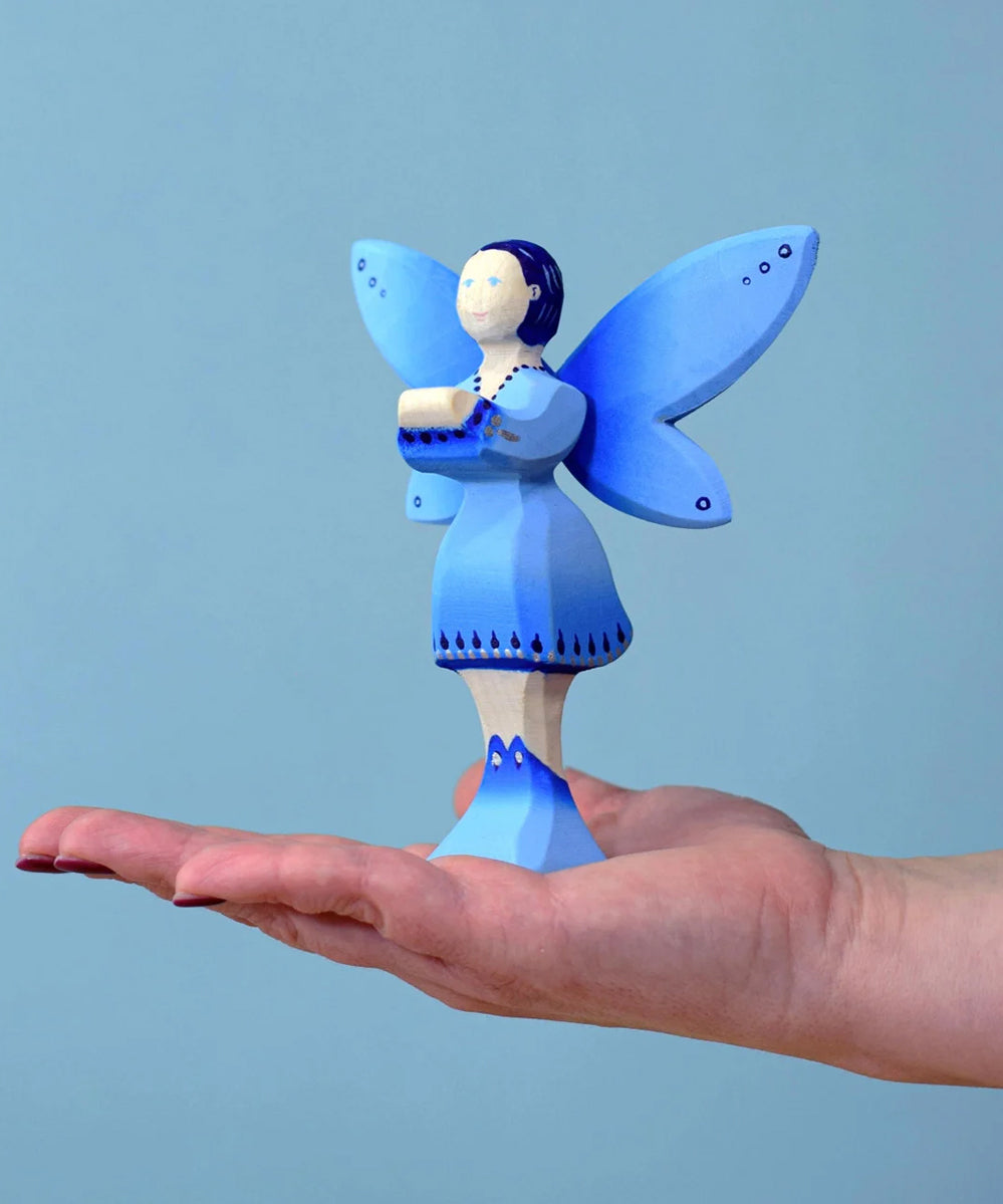 The Bumbu water fairy balanced on an adult's hand against a blue background.