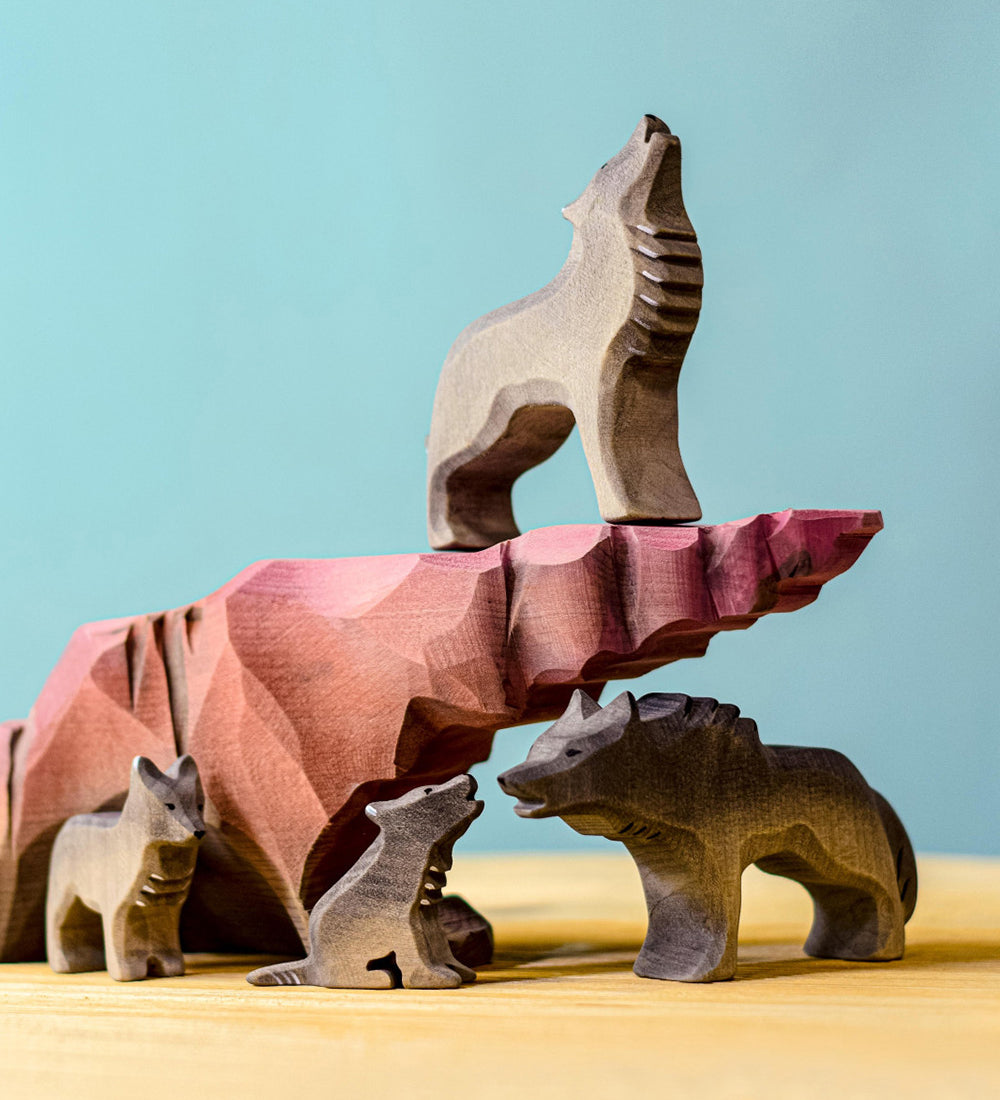 A collection of Bumbu wooden wolf figures sitting on and around a howling stone.