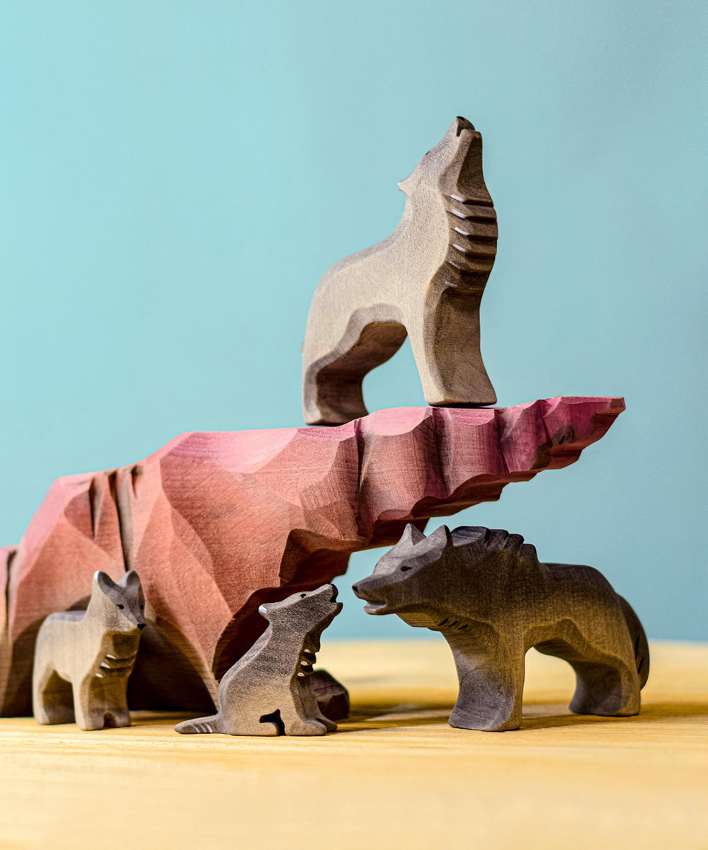 A collection of Bumbu wooden wolf figures sitting on and around a howling stone.