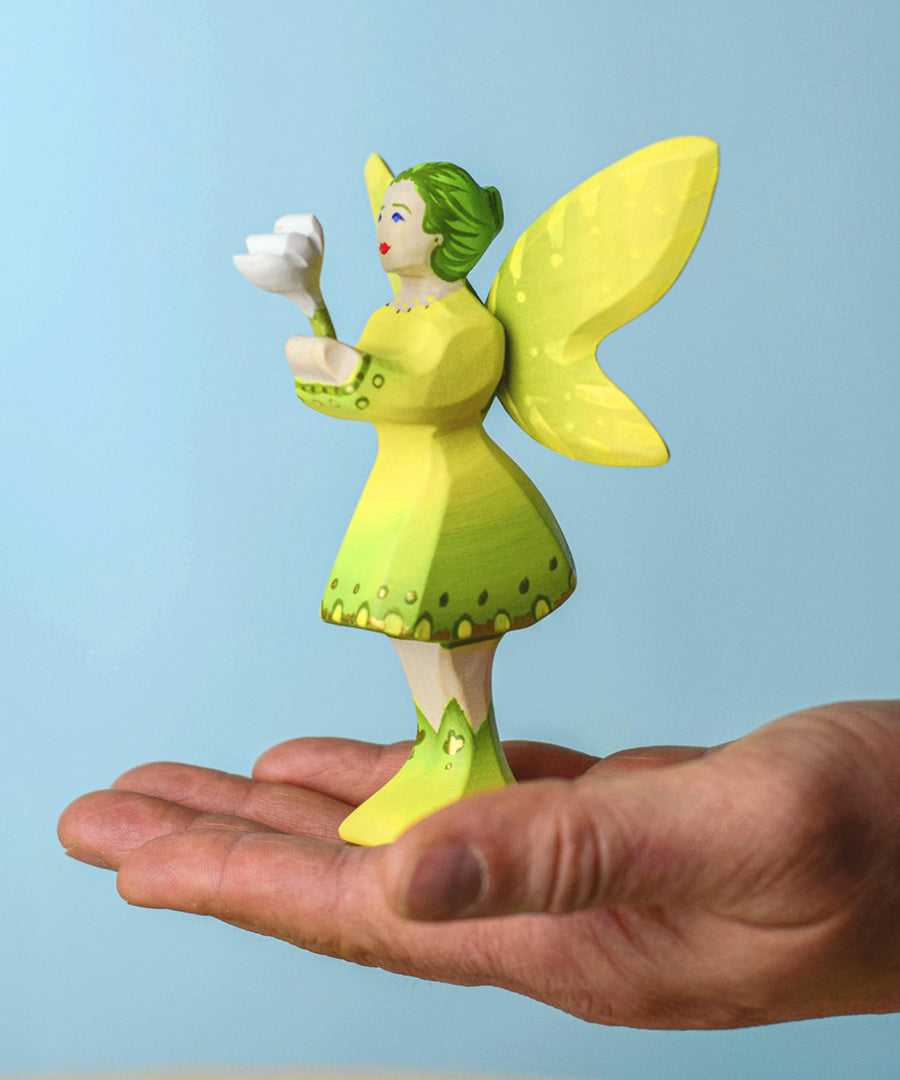 An adult balancing a Bumbu woodland fairy on thjeir hand. The fairy is holding onto a white flower .