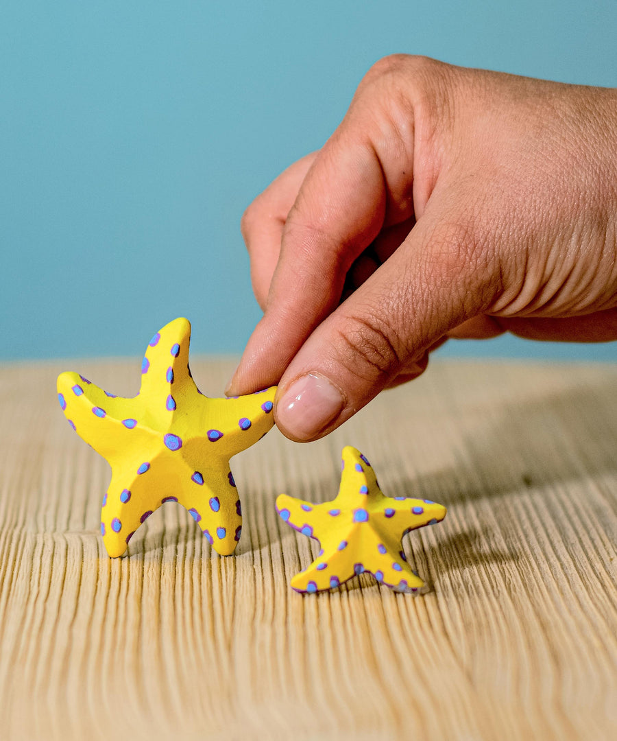 A close up of an adult's hand holding on to the large starfish from the Bumbu yellow starfish set.