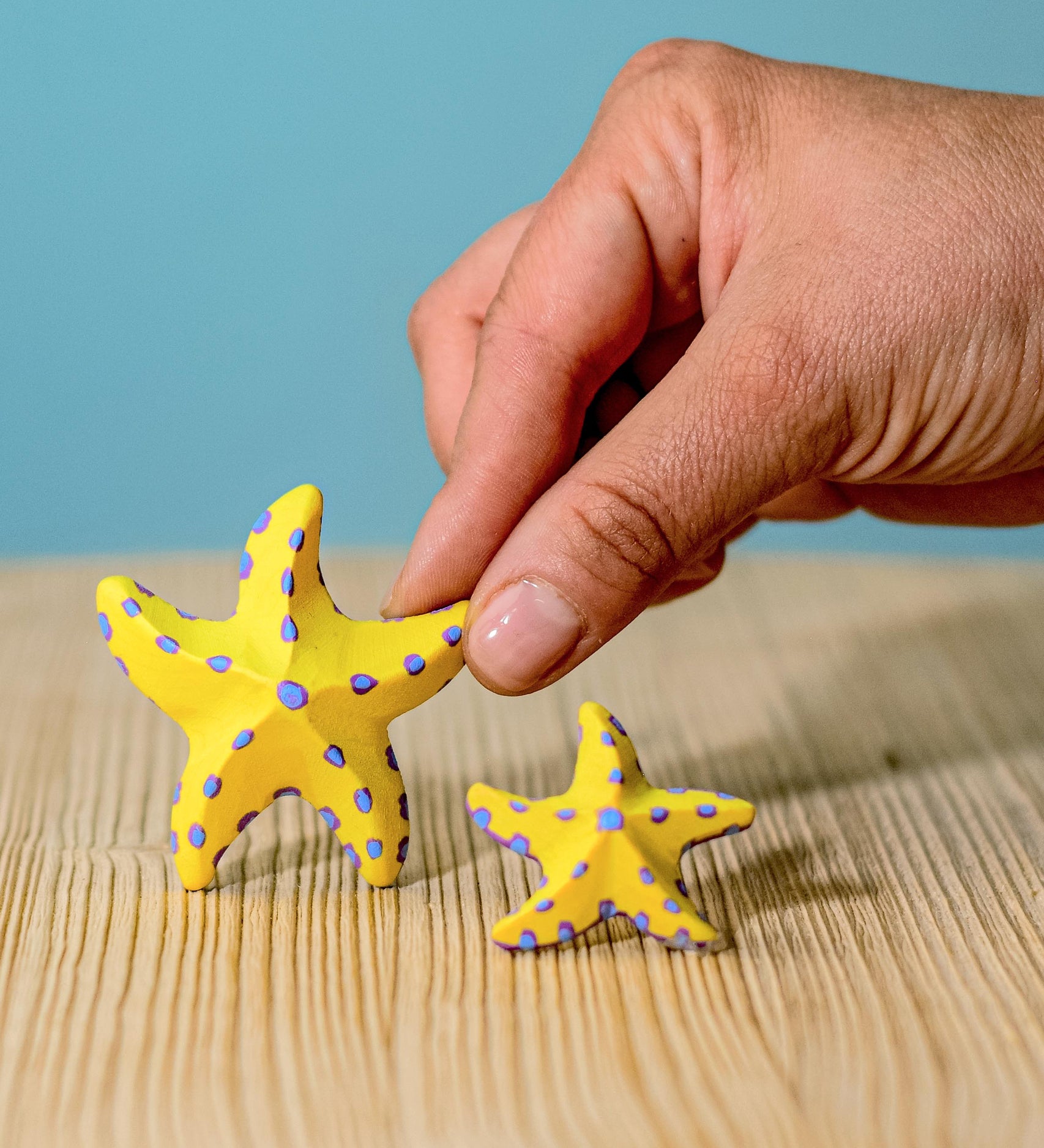 A close up of an adult's hand holding on to the large starfish from the Bumbu yellow starfish set.