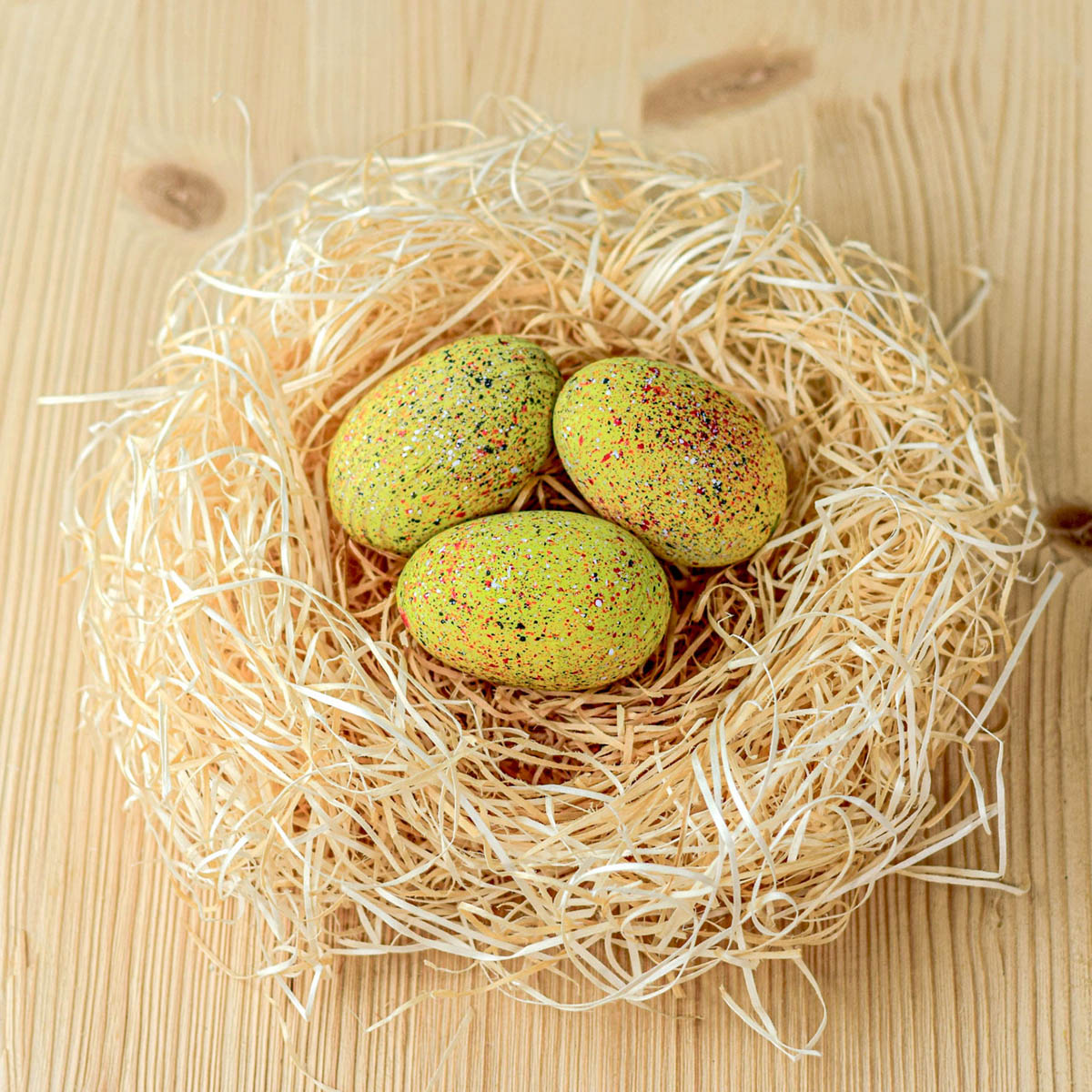 A birds-eye view of the Bumbu Wooden Stegosaurus Eggs Set. Three speckled yellow dinosaur eggs sat in a nest