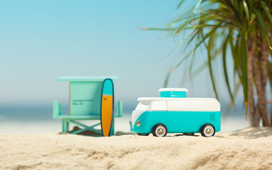 Candylab blue wooden beach van toy on some yellow sand in front of a palm tree