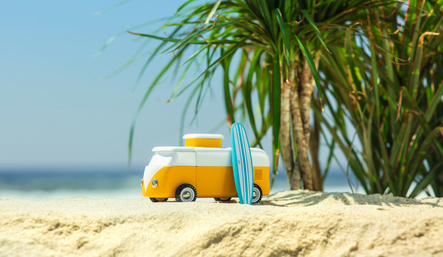 Close up of a Candylab sunset beach van toy on a sandy beach in front of some palm trees