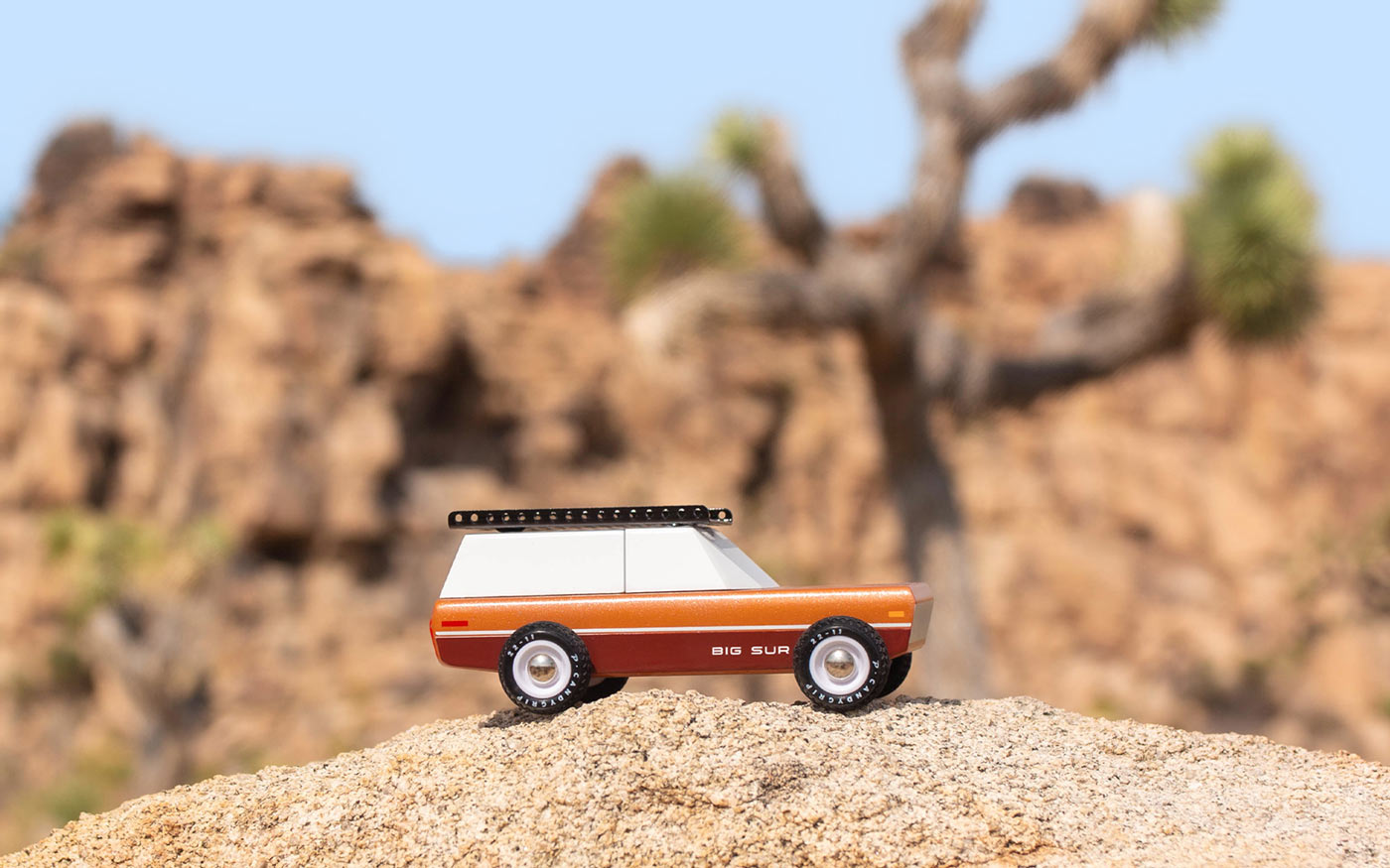 Candylab solid wooden vehicle toy on a large rock in front of a tree