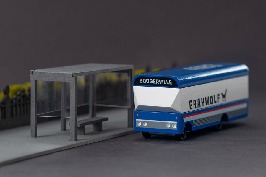 Candylab handmade wooden diecast bus toy on a grey background next to a miniature bus stop