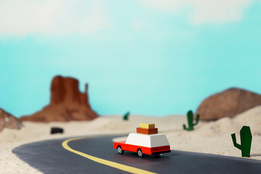 Candylab wooden luggage wagon collectable car toy on a rubber road in front of a rocky landscape