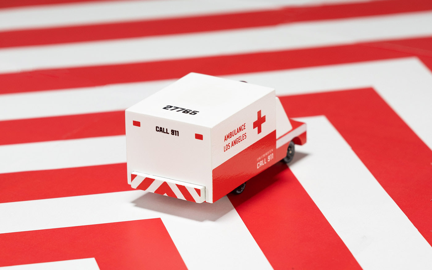 Candylab childrens small wooden ambulance toy on a red and white striped background