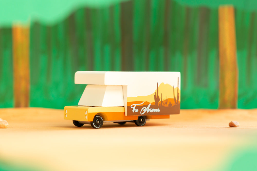 Close up of the Candylab childrens arizona campervan toy on a yellow background in front of some paper trees