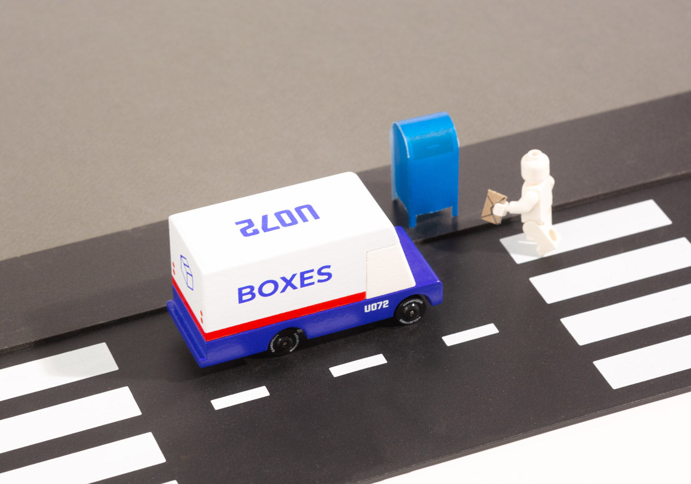 Close up of a Candylab wooden post van next to a toy mailbox and toy figure on a black rubber road