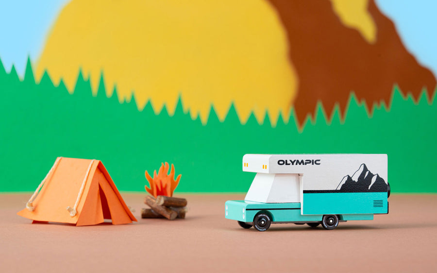 Candylab collectable diecast rv toy next to a paper tent in front of a yellow mountain background